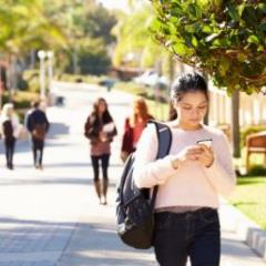 Female university student scrolling phone walking to class